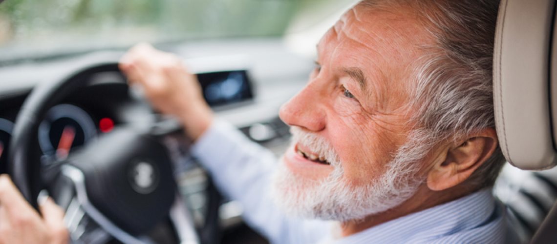 A close-up of happy senior man sitting in car in driver seat, driving.