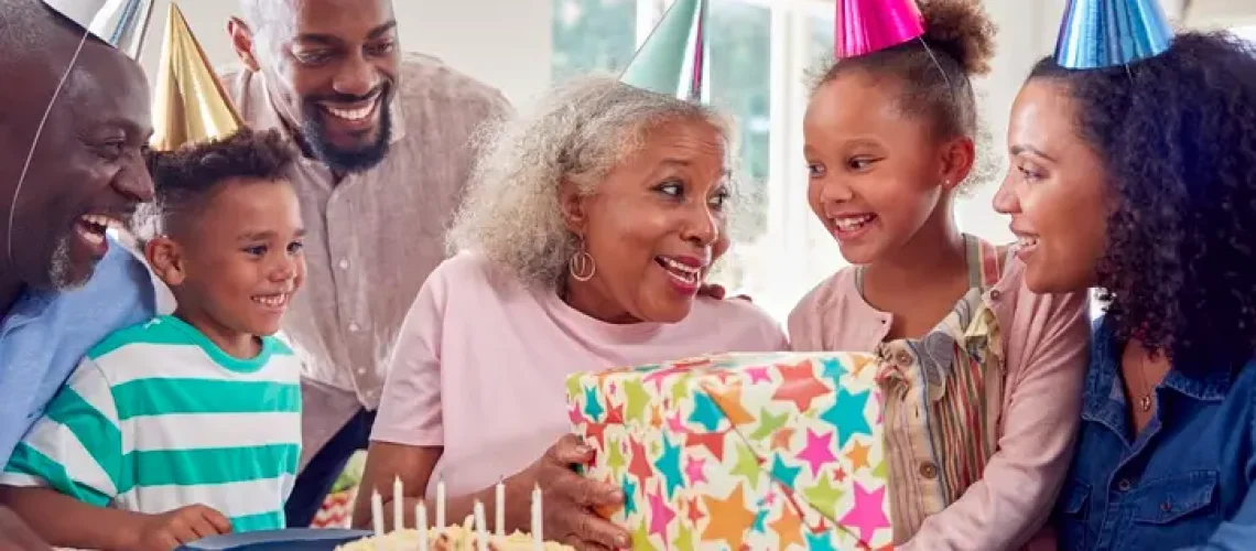 Multi Generation Family Around Table At Home Celebrating Grandmother's Birthday With Cake And Party